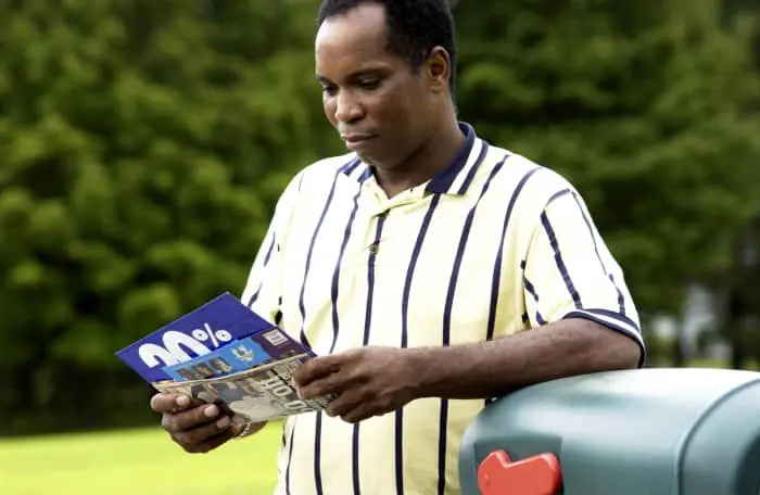 A man getting mail from his outdoor mailbox and looking through postcards and envelopes.