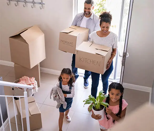 Family of four enters their new home carrying moving boxes.