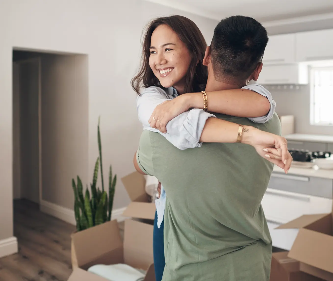 Ethnic family with two children carrying boxes and plant in new home on moving day. High angle view of happy smiling daughters helping mother and father with cardboard boxes in new house. Top view of excited kids having fun walking up stairs running to their rooms while parents holding boxes.