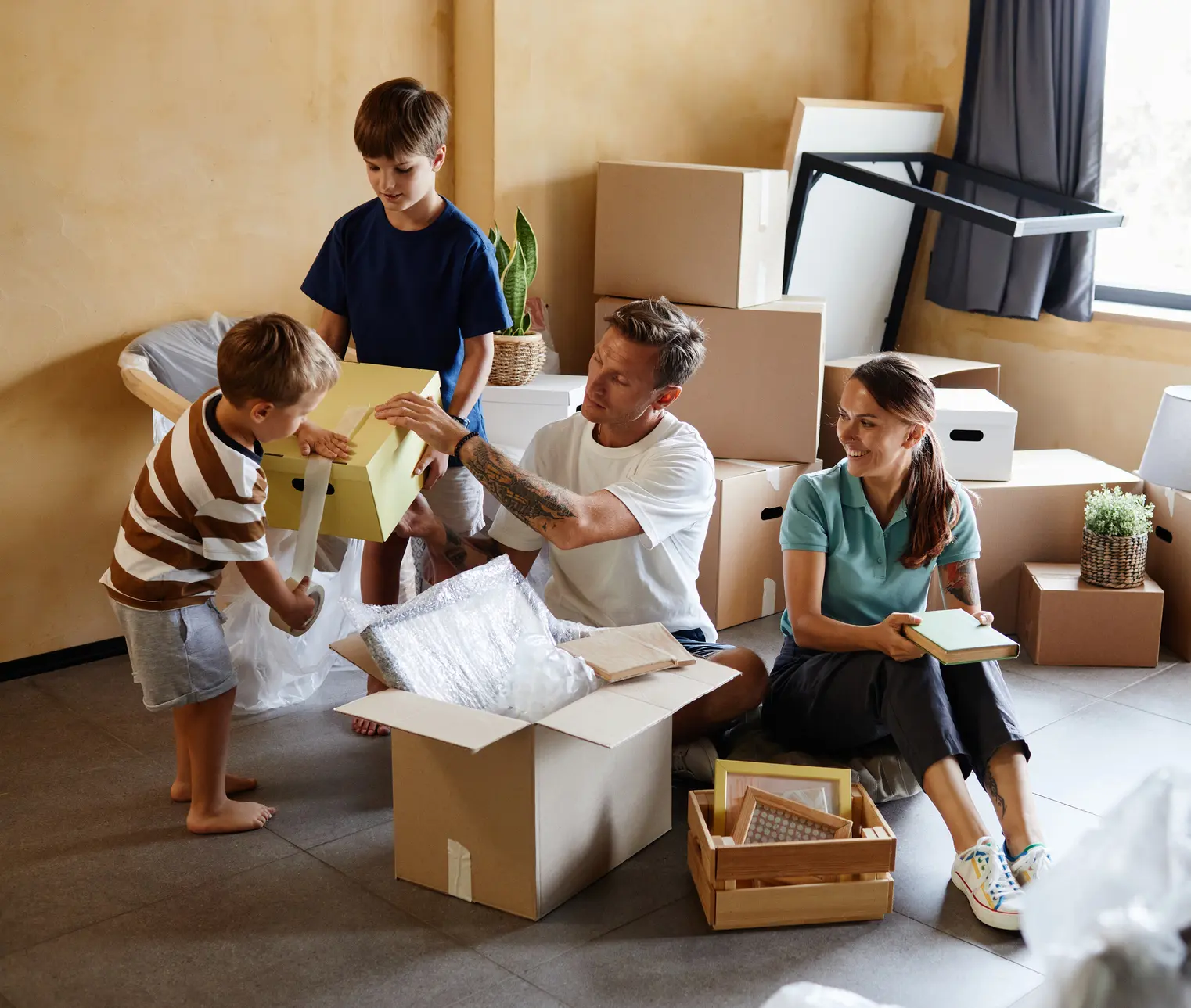 A family of four sitting down packing boxes preparing to move into their new home