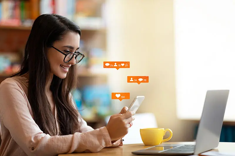 Woman on her phone at the dinner table with a yellow tea cup checking social media engagement