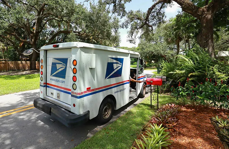 Mail carrier puts Direct Mail in a red mailbox in a tropical area.