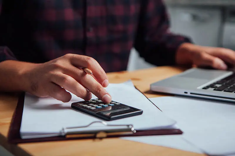 Man with plaid shirt with computer and calculator. Understanding the cost involved in a Direct Mail campaign.