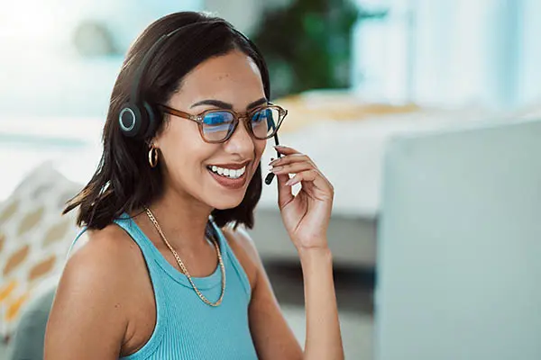 Woman wearing a blue top and glasses is working from home on a computer while working on a direct mail marketing campaign