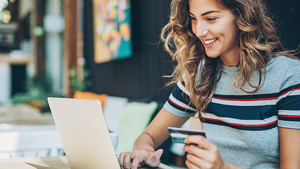 Woman on a computer purchasing because of information she read on a Direct Mail postcard marketing piece