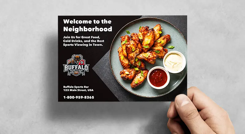 a hand holding a postcard that says welcome to the neighborhood and has a plate of buffalo wings for a local sports bar