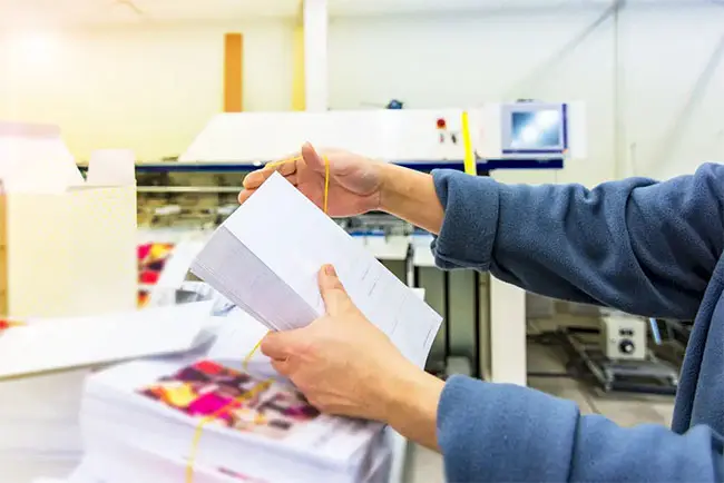 A person with a blue long sleeved shirt grabbing a stack of direct mail with a focus on whitespace